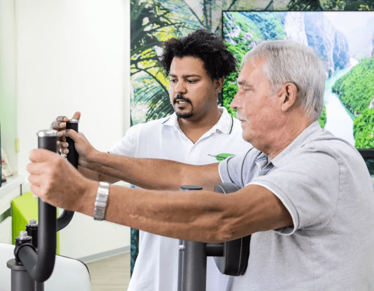 Steven Kato erklärt älterem Herr eine Übung am Fitnessgerät